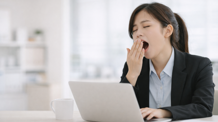 업무 중 노트북 앞에서 식후 졸음을 느끼는 젊은 직장인 여성